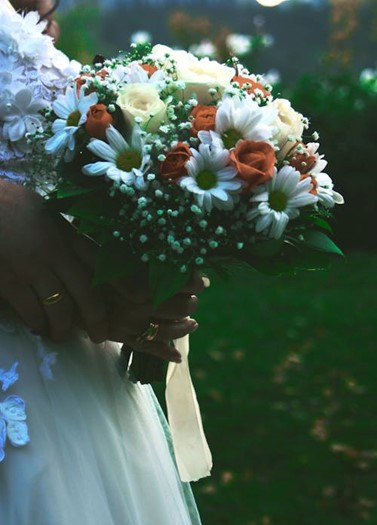 Een bruid heeft een bruidsboeket vast met witte en oranje bloemen.